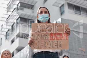 The choice is yours. Low angle shot of an attractive young woman holding up a sign protesting against the covid 19 vaccine with other demonstrators in the background.