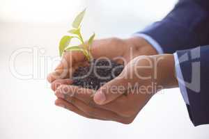 Sometimes, a promise comes from dirt. an unrecognizable businessman holding a plant growing out of soil.