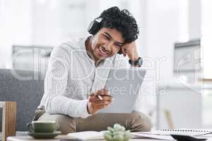 His connections allow him to achieve so much more. a young businessman wearing headphones while using a digital tablet in an office.