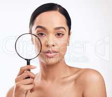 Its time to take action and protect your skin. a beautiful young woman holding a magnifying glass while posing against a white background.