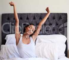 A good nights sleep makes me feel like I can conquer anything. a young woman stretching in her bed after waking up.