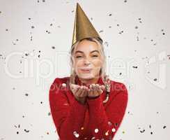 The world has grown weary through the years, but at Christmas it is young. Studio shot of a young woman wearing a party hat and blowing confetti against a grey background.