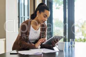I dont need to go out to pay bills, I do it online. a young woman standing in her kitchen with paperwork and a digital tablet.