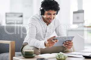 Its his business gadget of choice. a young businessman wearing headphones while using a digital tablet in an office.