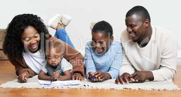 Letting his creativity run wild. a two young parents lying on the living room floor with their children and watching them draw.