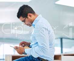 Our schedule is filling up fast. a handsome young businessman sitting alone in his office and using a digital tablet.