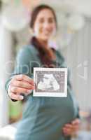 Ive been staring at you for ages. a young mother to be holding an ultrasound of her unborn child.