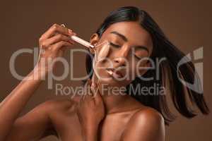 Sideways for attention, longways for results. an attractive young woman using a derma roller against a brown background.