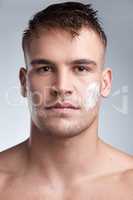 Getting down to the nitty gritty. Cropped closeup portrait of an attractive young man applying moisturiser to his face against a grey background.