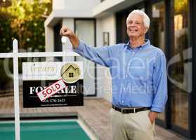 Ive got the keys to my kingdom. Cropped portrait of a handsome senior man standing next to a sold sign and holding the keys up proudly outside of his newly purchased home.