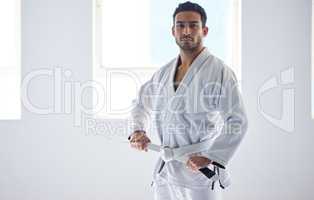 Starting my jiu jitsu journey. Cropped portrait of a handsome young male martial artist tying his belt in the gym.