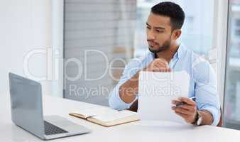 Making sure he understands all the conditions. a young businessman going through paperwork while working on a laptop in an office.