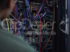 Lets organize this cabling. an unrecognizable male IT support agent working in a dark network server room.