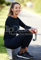 Eating healthy keeps me in shape. Full length portrait of an attractive and athletic young woman sitting on the curb with her apple and water bottle.