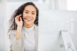Ill assist with your query. Portrait of a young businesswoman wearing a headset while working on a computer in an office.