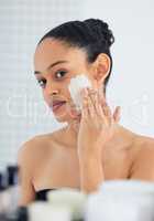 Time to shrink those pores. an attractive young woman standing alone in her bathroom at home and applying a face mask.