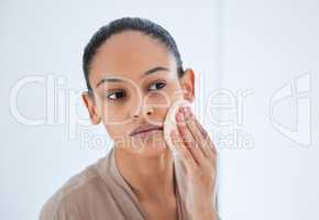 I never neglect my skin. an attractive young woman standing alone in her bathroom and home and cleansing her skin.