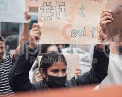 Fight covid. an attractive young woman holding up a sign protesting against the covid 19 vaccine with other demonstrators in the background.