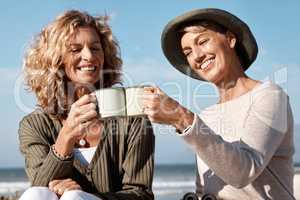 Cheers to the good life. two attractive mature women enjoying some coffee while sitting on the beach.