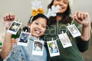 Decorate your home with happy family memories. a happy young mother and daughter hanging up family photographs during Christmas at home.