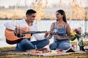 Life is a song, love is the music. a young man playing a guitar while on a picnic with his girlfriend at a lakeside.