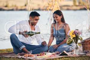 Celebrating their anniversary at their favourite picnic spot. a young couple drinking champagne while on a picnic at a lakeside.
