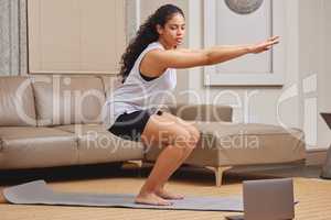 Online fitness classes are the best. Full length shot of a young woman using her laptop to follow an online fitness class in her living room.