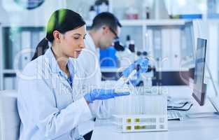 Each dosage, carefully measured. an attractive young female scientist working in her lab with a colleague in the background.