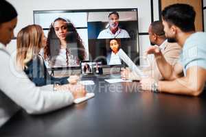 Connecting with colleagues around the globe. a diverse group of businesspeople sitting in the boardroom during a meeting with their international colleagues via video chat.