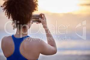 Capture every moment. a young woman taking a photo of the sunset.