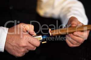 Treat yourself to the finer things in life. an unrecognizable man lighting a cigar with a lighter.