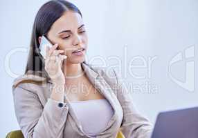 Sorting out a few of her big plans. a young businesswoman talking on a cellphone while working on a laptop in an office.