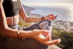 The best cure for the body is a quiet mind. a young woman meditating while sitting on a mountain cliff.