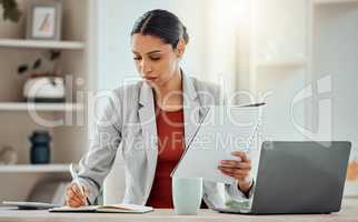 African Business woman planning, taking notes and writing in a notebook while reading a report, document or paperwork in an office alone at work. One serious corporate professional working at a desk