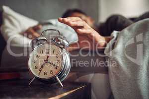 Early to bed, early to rise. a young man reaching for his alarm clock after waking up in bed at home.