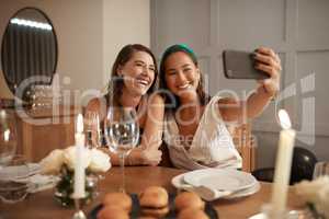 Its a bestie selfie only. two young friends sitting together and using a cellphone to take selfies during a New Years dinner party.