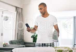 Multitasking is hard sometimes. a young man ironing clothes while using a phone at home.
