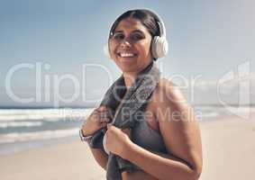 Exercise brings out the best in me. a sporty young woman wearing headphones and a towel around her neck on the beach.
