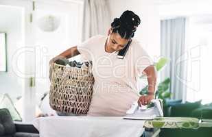 So much to do and so little time. a young woman ironing clothes while on the phone at home.