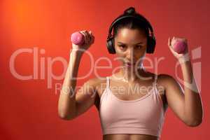 You earn it through a lot of hard work. Studio portrait of a sporty young woman exercising with dumbbells against a red background.