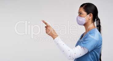 Gave up my life to learn how to save yours. Side shot of a young doctor wearing a surgical face mask and pointing to her right against a white background.