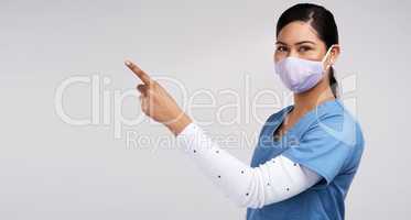 Working for cause, keep your applause. Portrait of a young doctor wearing a surgical face mask and pointing to her right against a white background.