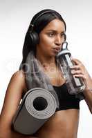 Sip water at regular intervals while exercising. Studio shot of a sporty young woman drinking water and holding a yoga mat against a white background.