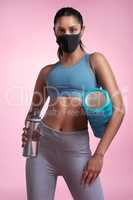 Quitting is never an option. Cropped portrait of an attractive and sporty young woman wearing a mask while posing with a foam roller and water bottle in studio against a pink background.