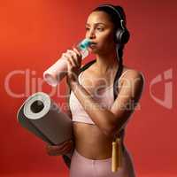 Its not always easy, but its always worth it. Studio shot of a sporty young woman drinking water and holding a yoga mat against a red background.