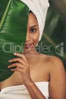 Feed your skin nothing but goodness. a beautiful young woman wearing a towel around her head while posing behind a green leaf.