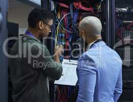 Explaining the ins and outs. two male IT support agents working together in a dark network server room.