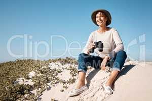 She loves a little sightseeing at the beach. Full length shot of an attractive mature woman using her binoculars while sitting on the beach.