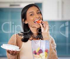 Choose foods that nourish your body. a young woman eating a strawberry while preparing a healthy smoothie at home.