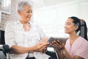 Guided recovery. a young nurse sharing information from her digital tablet with an older woman in a wheelchair.